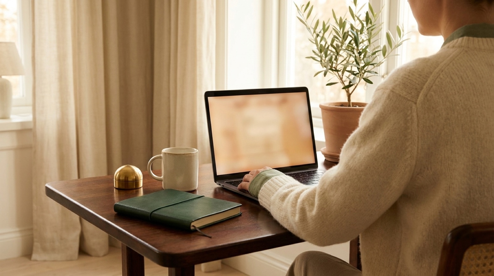 A person reviewing a real-estate listing on a laptop at a wooden desk with coffee and a notebook nearby